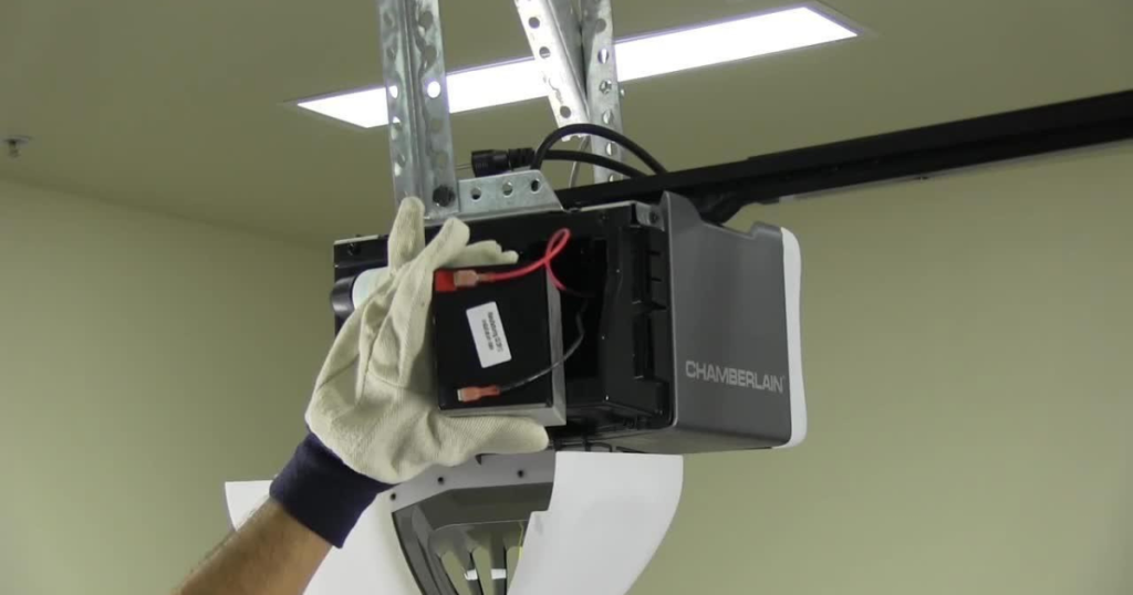 Gloved hand installs garage opener battery.